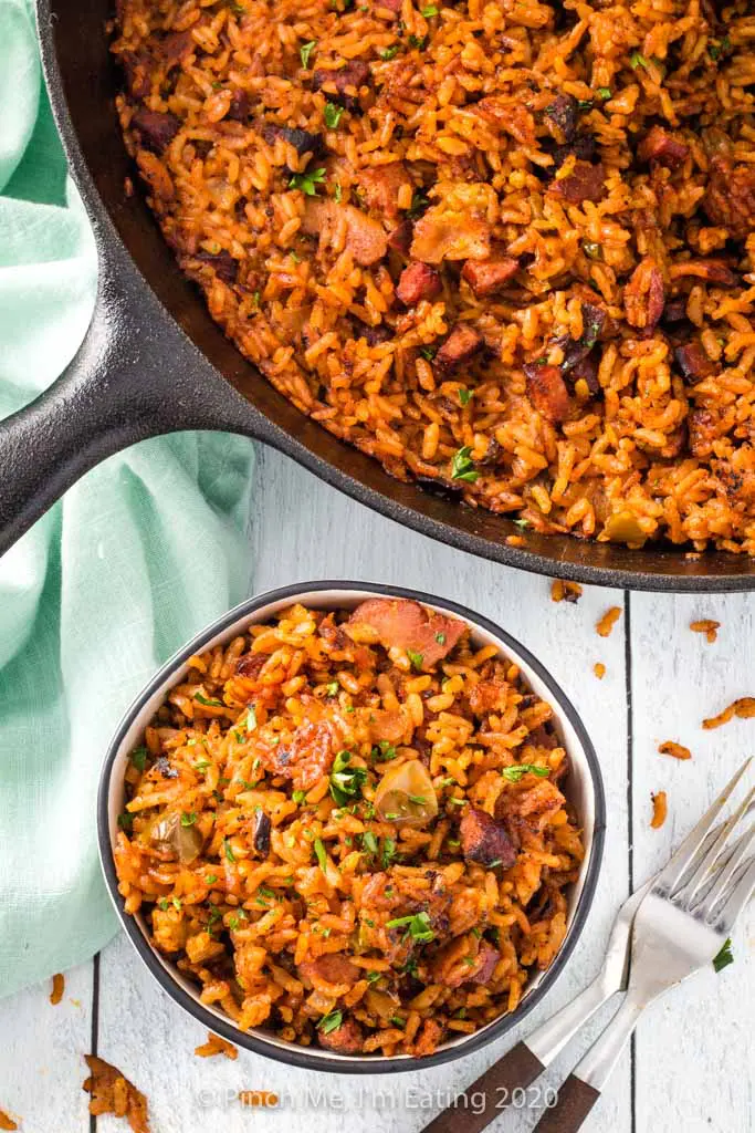 Overhead view of Charleston red rice with bacon and sausage in a cast iron skillet and small bowl with two forks