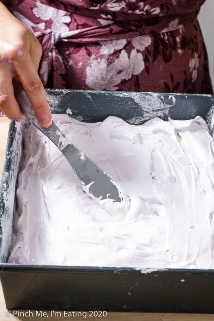 A woman uses a knife to marbleize purple and white homemade marshmallow mixture in a baking pan