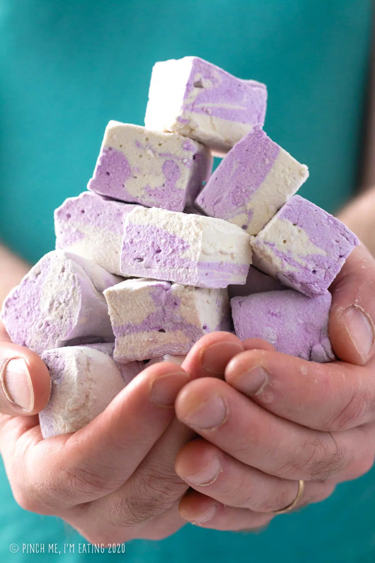 Cupped hands holding a mount of purple and white swirled homemade Earl Grey marshmallows in front of an aqua shirt.