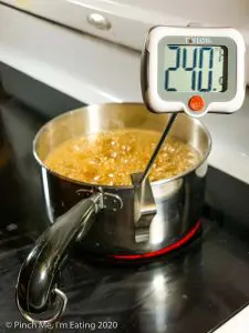A small saucepan of boiling sugar syrup with a digital candy thermometer reading 240 degrees.