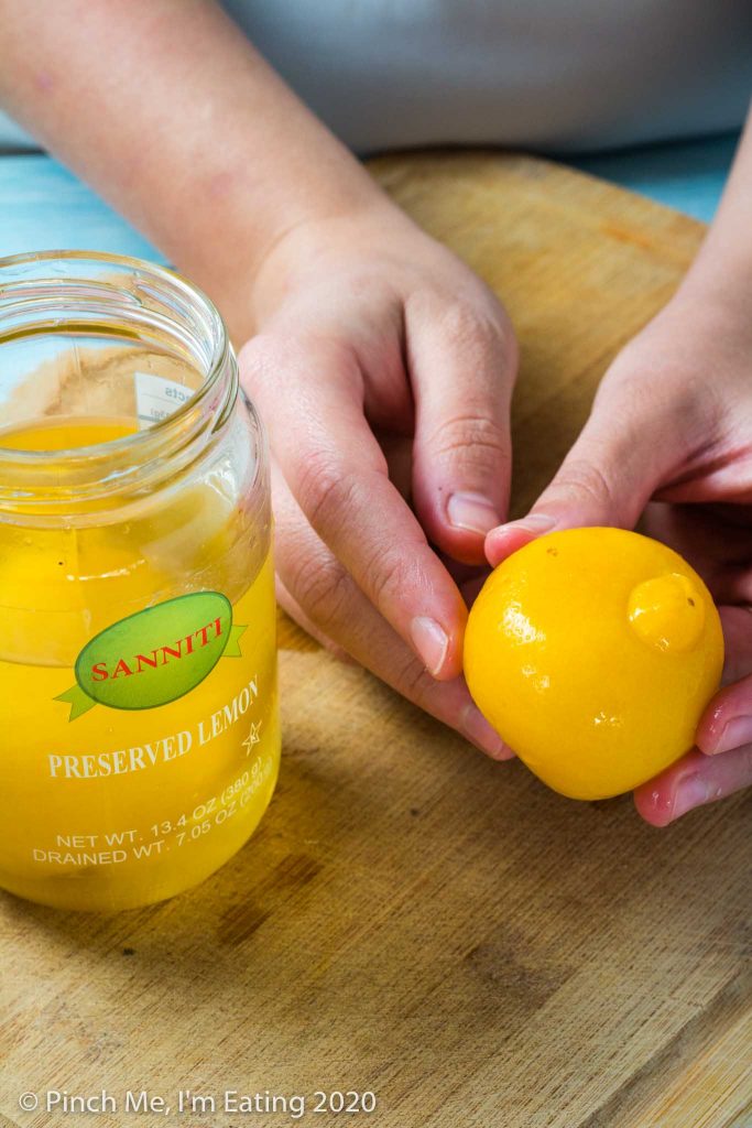 hands holding a preserved lemon next to a jar of preserved lemons on a wooden cutting board