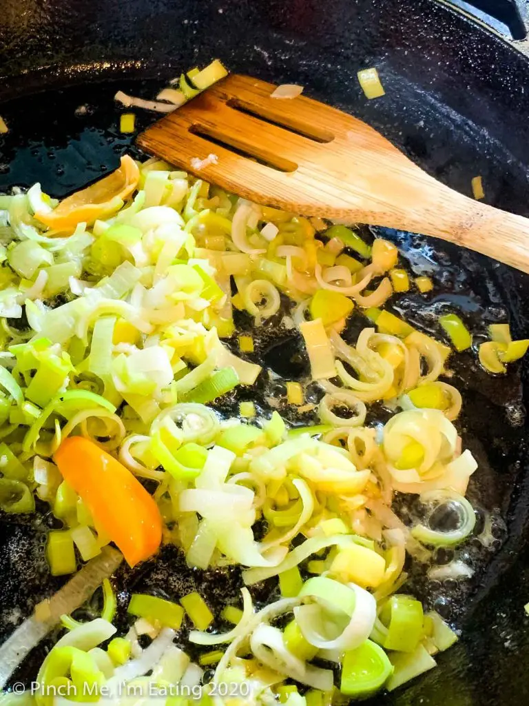 Leeks sautéing in a cast iron skillet with large pieces of habanero pepper