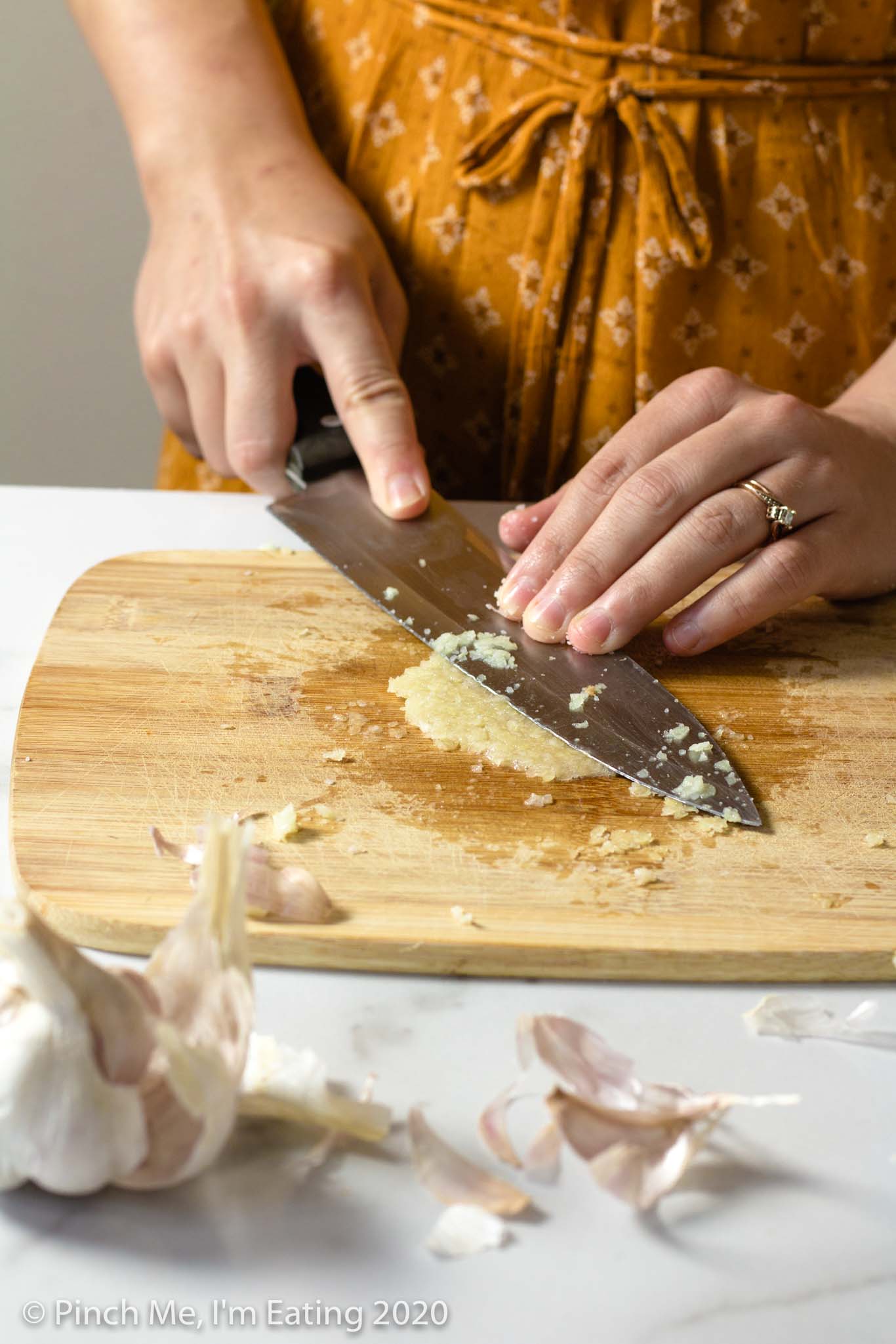 Woman smashing garlic onto wooden cutting board with the flat side of a chef's knife