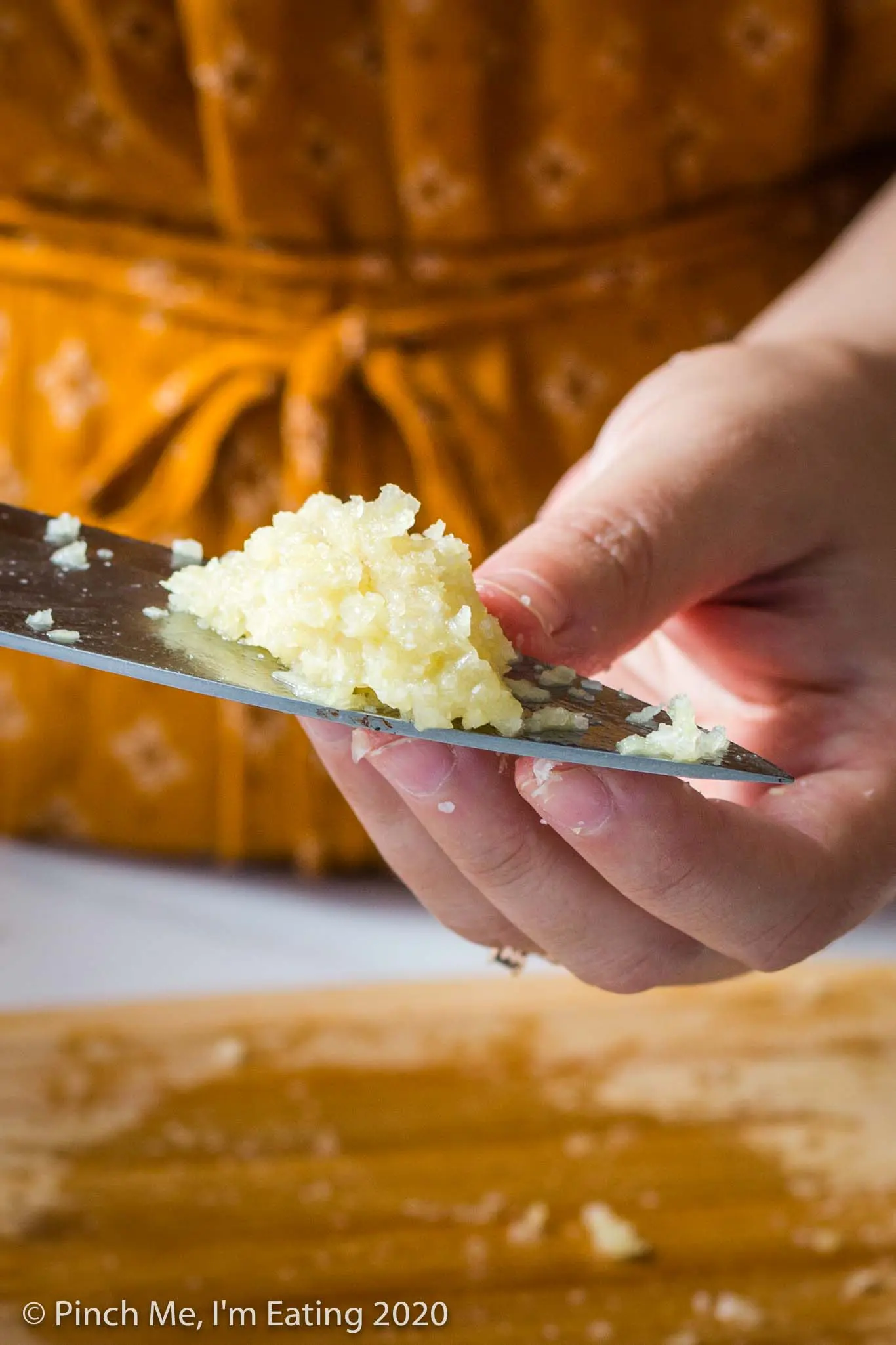 Woman holding garlic paste on the side of a knife.