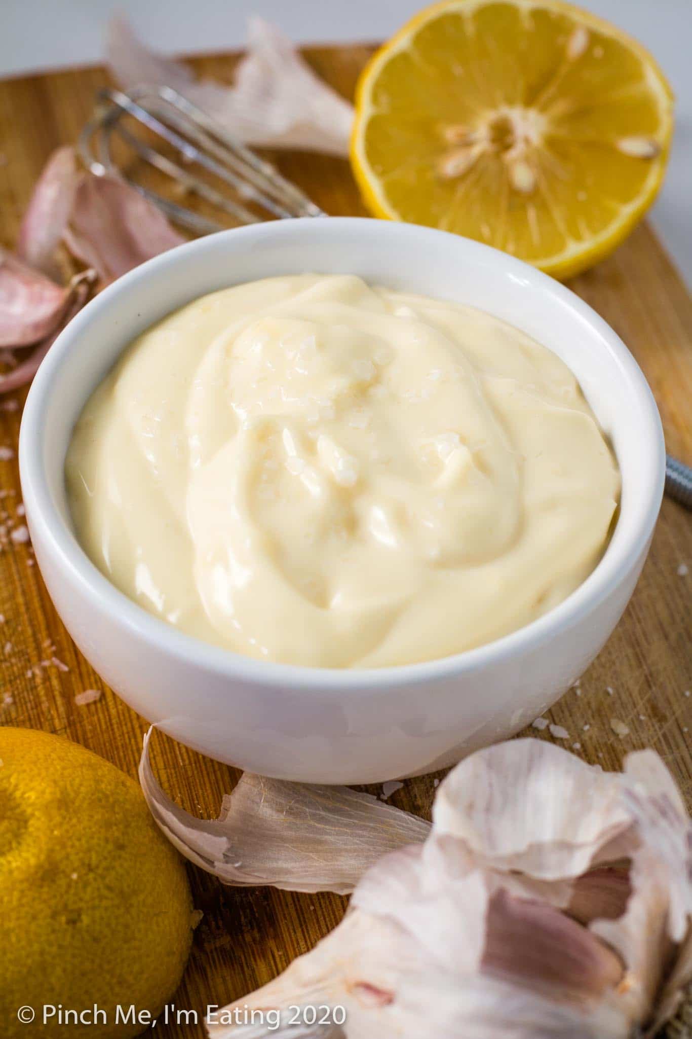 Easy garlic aioli in a small white bowl with a lemon and whisk in the background