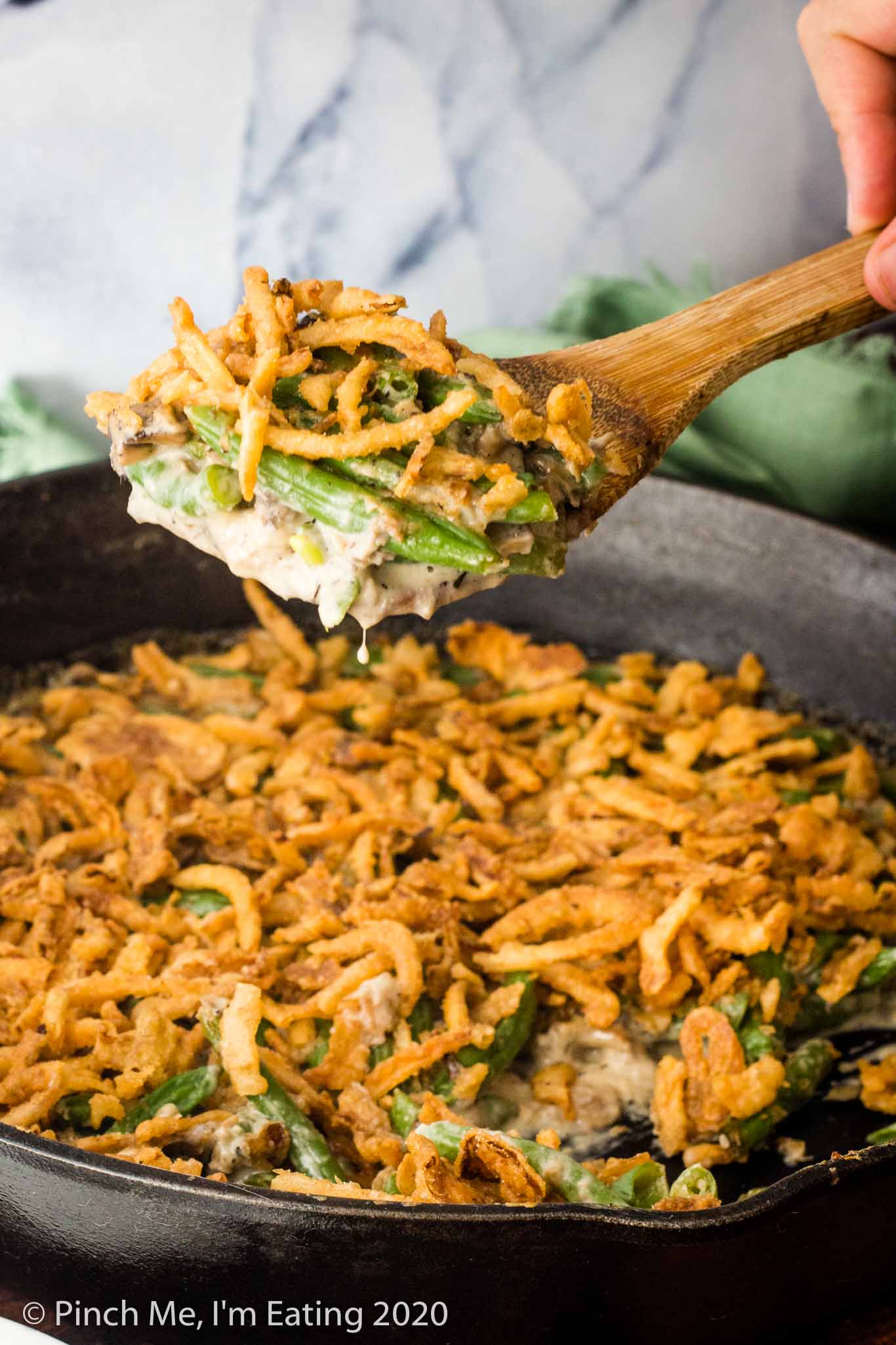 A wooden spoon serving fresh green bean casserole out of a cast iron skillet