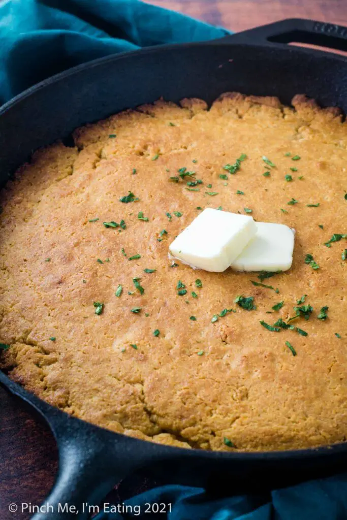 Buttermilk cornbread in a cast iron skillet with two pats of butter and parsley on top
