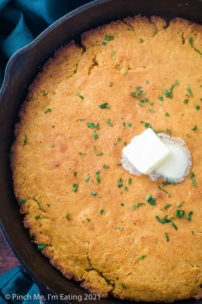 Overhead view of buttermilk cornbread in a cast iron skillet topped with butter