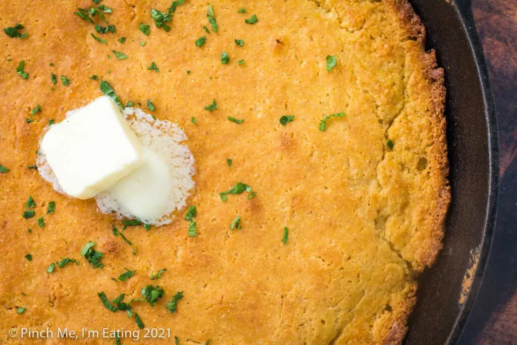 Overhead view of Southern buttermilk cornbread in a cast iron skillet topped with butter