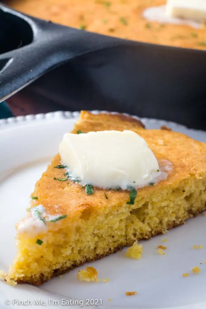 A wedge of Southern buttermilk cornbread on a white plate with butter on top