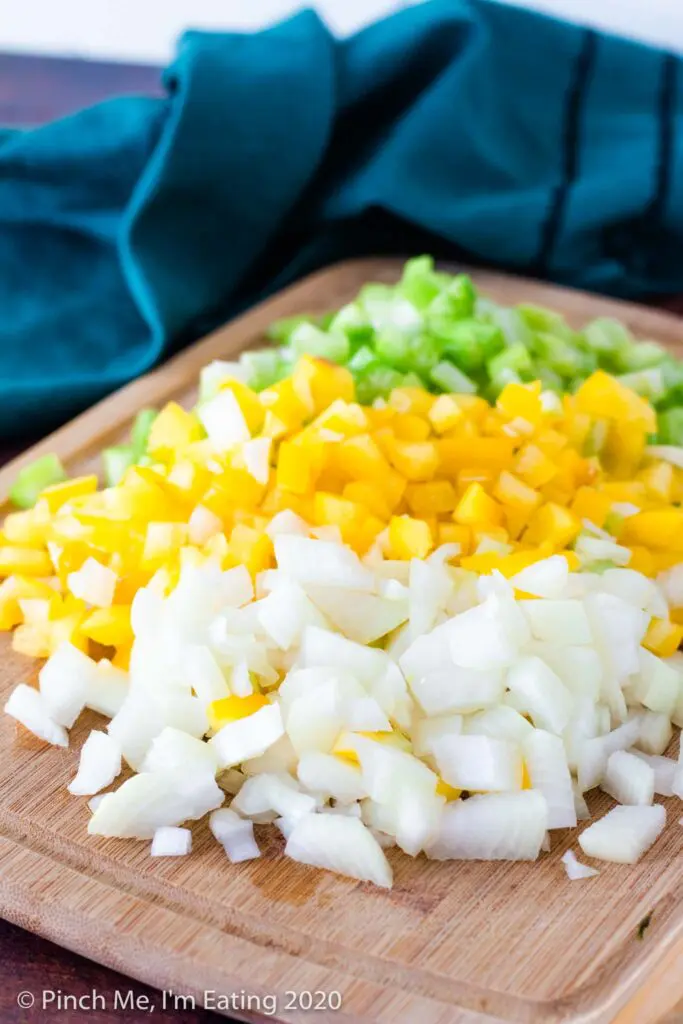 Wooden cutting board with diced onions, yellow bell pepper, and celery