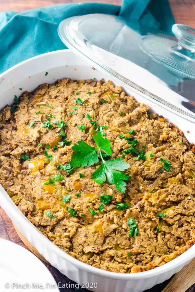 Three quarter view of Southern cornbread dressing in a white casserole dish with glass lid propped on the side