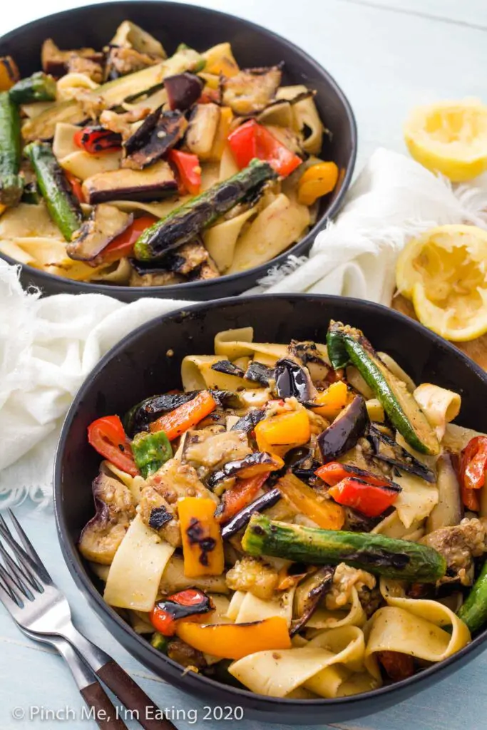 Two black bowls of pappardelle pasta with grilled vegetables