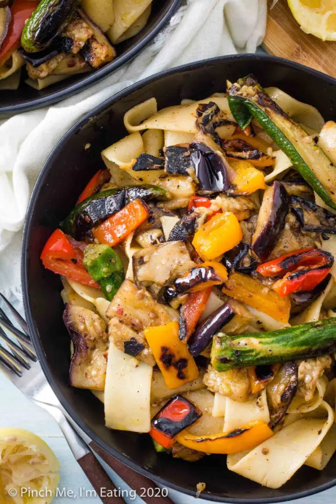 A black bowl of pappardelle pasta with grilled eggplants, bell peppers, and baby zucchini
