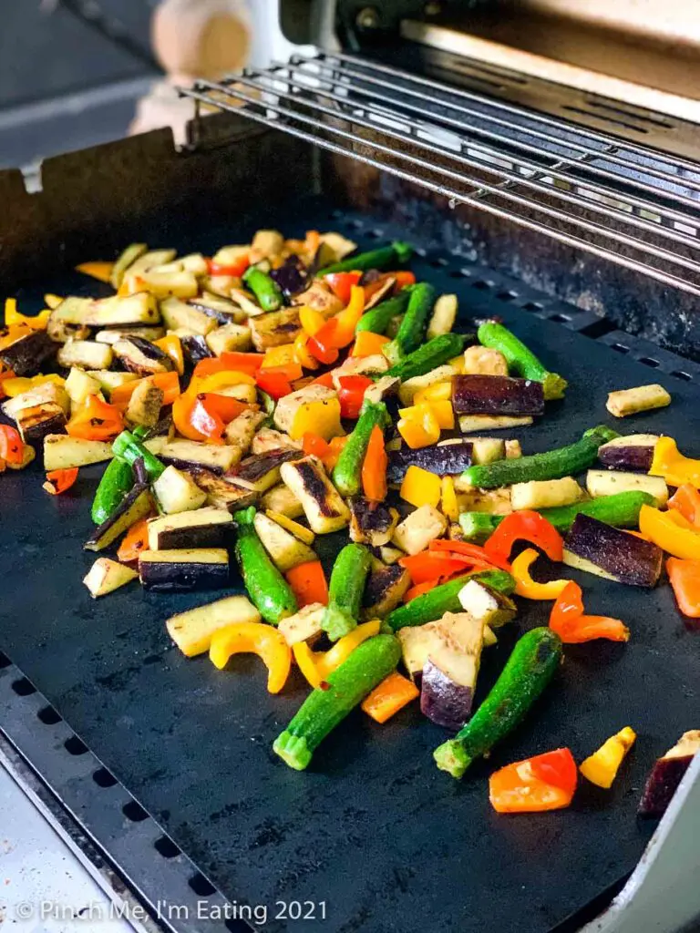Cut vegetables sautéeing on grill mats on a Weber grill