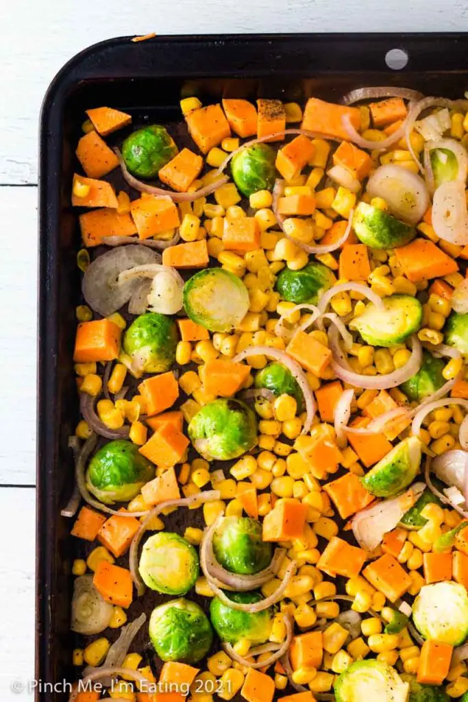 Sheet pan of cut Brussels sprouts, diced sweet potatoes, shallots, and corn