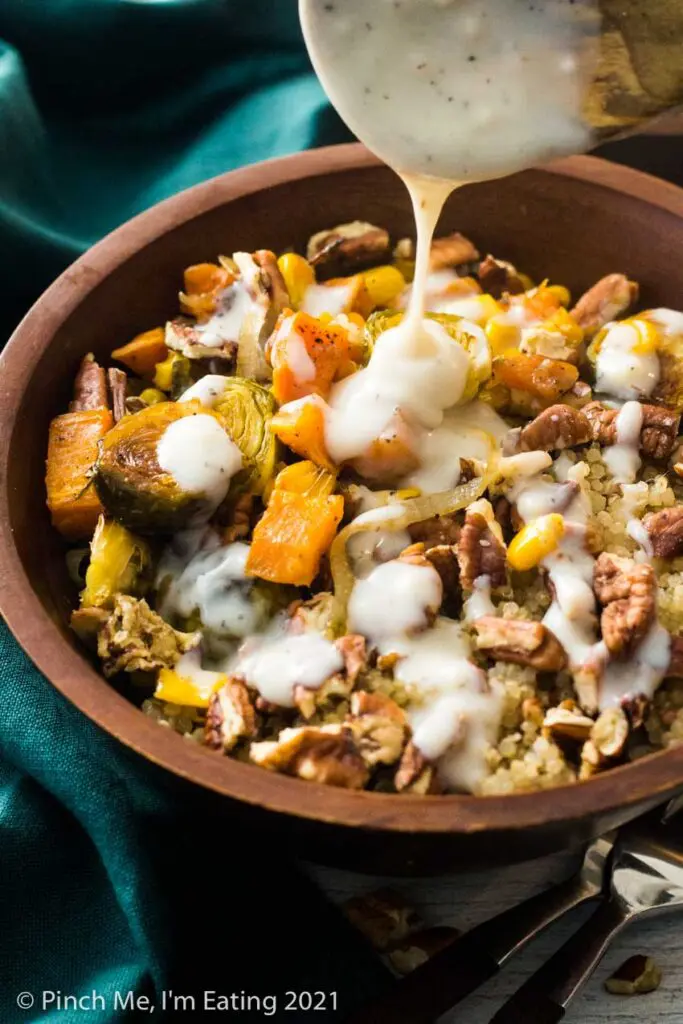 Creamy mozzarella sauce being drizzled over a roasted vegetable quinoa harvest bowl with Brussels sprouts, quinoa, corn, sweet potatoes, shallots, and pecans