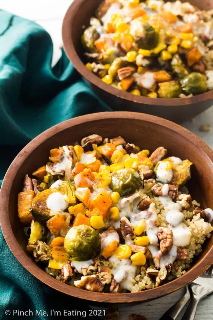 Two roasted vegetable quinoa harvest bowls in wooden bowls with Brussels sprouts, quinoa, corn, sweet potatoes, shallots, pecans, and a creamy mozzarella sauce