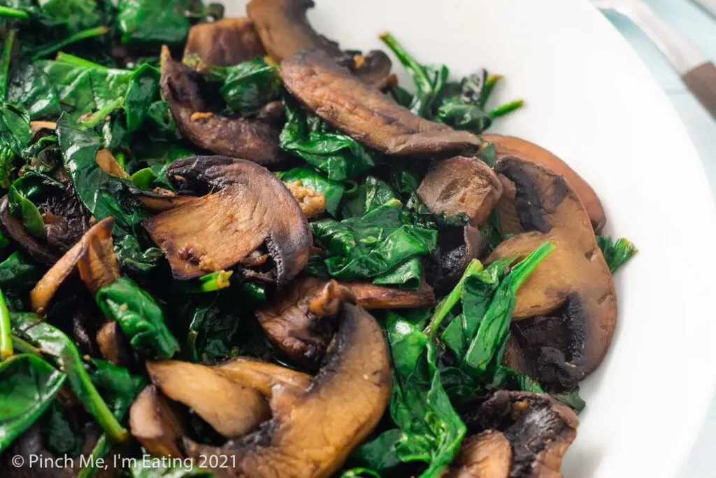 Close up of sautéed spinach and browned mushrooms in a white bowl