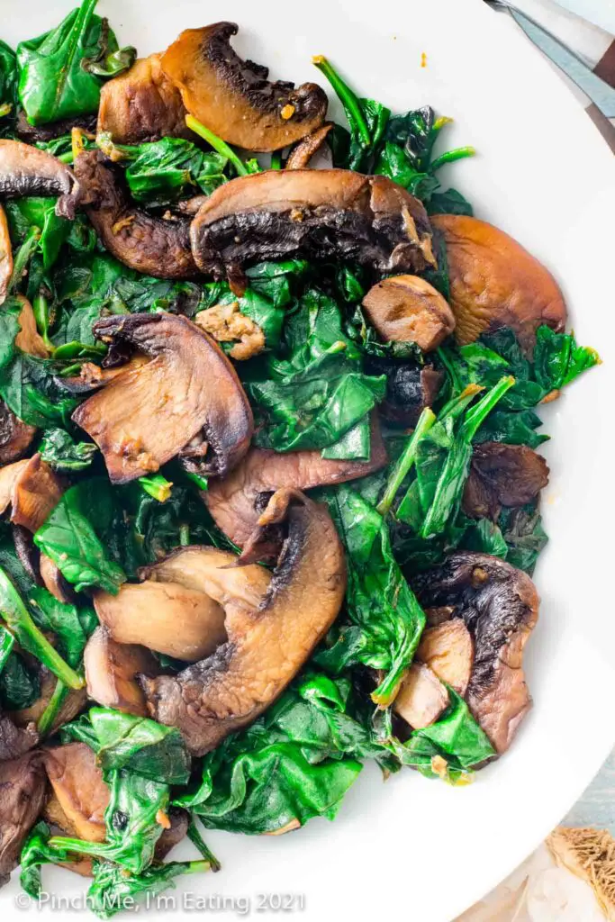 Close up overhead view of sautéed spinach and mushrooms in a white bowl