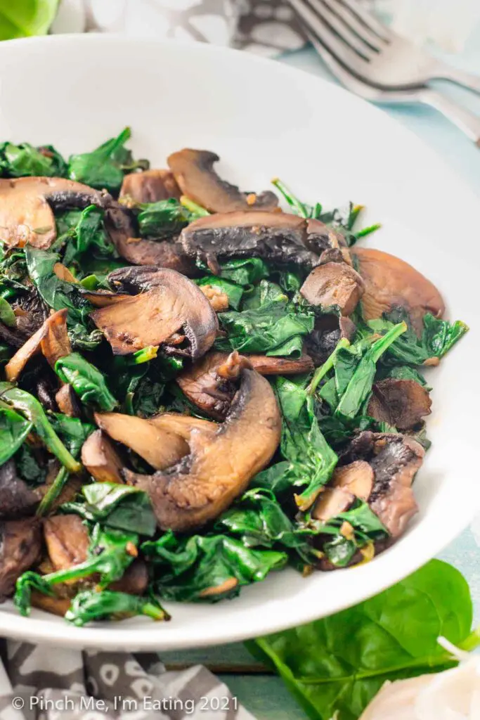 Three quarter view of sautéed spinach and browned mushrooms in a white bowl