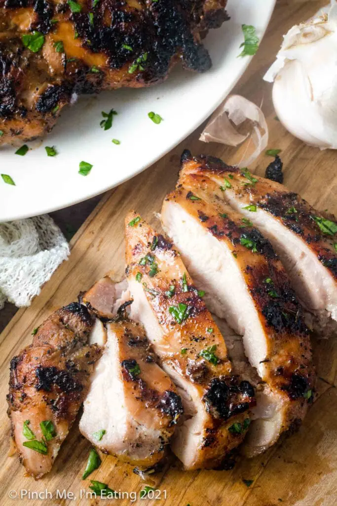 Overhead view of grilled balsamic chicken sliced into strips on a wooden cutting board