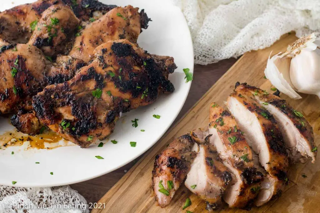Overhead view of grilled balsamic chicken thighs on a white plate and a sliced piece of chicken on a wooden cutting board