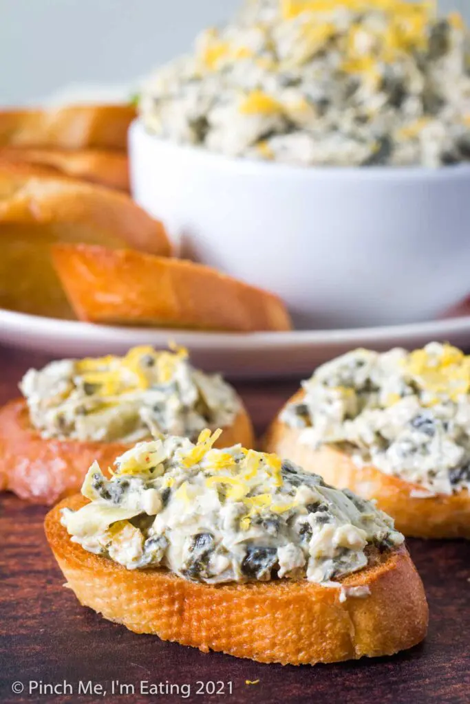 Crostini topped with cold artichoke spinach dip with lemon zest