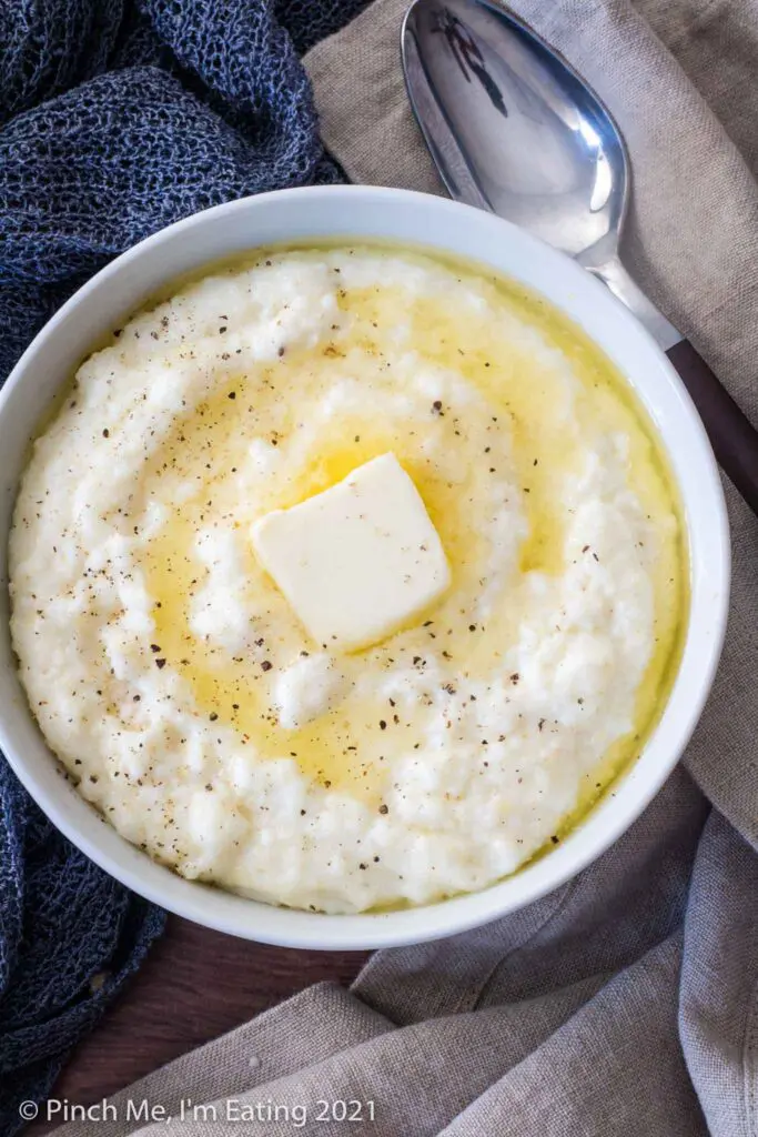 Overhead view of white bowl of creamy Southern grits with melting butter next to a spoon