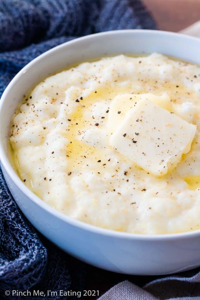 Three quarter view of white bowl of creamy Southern grits with butter and black pepper