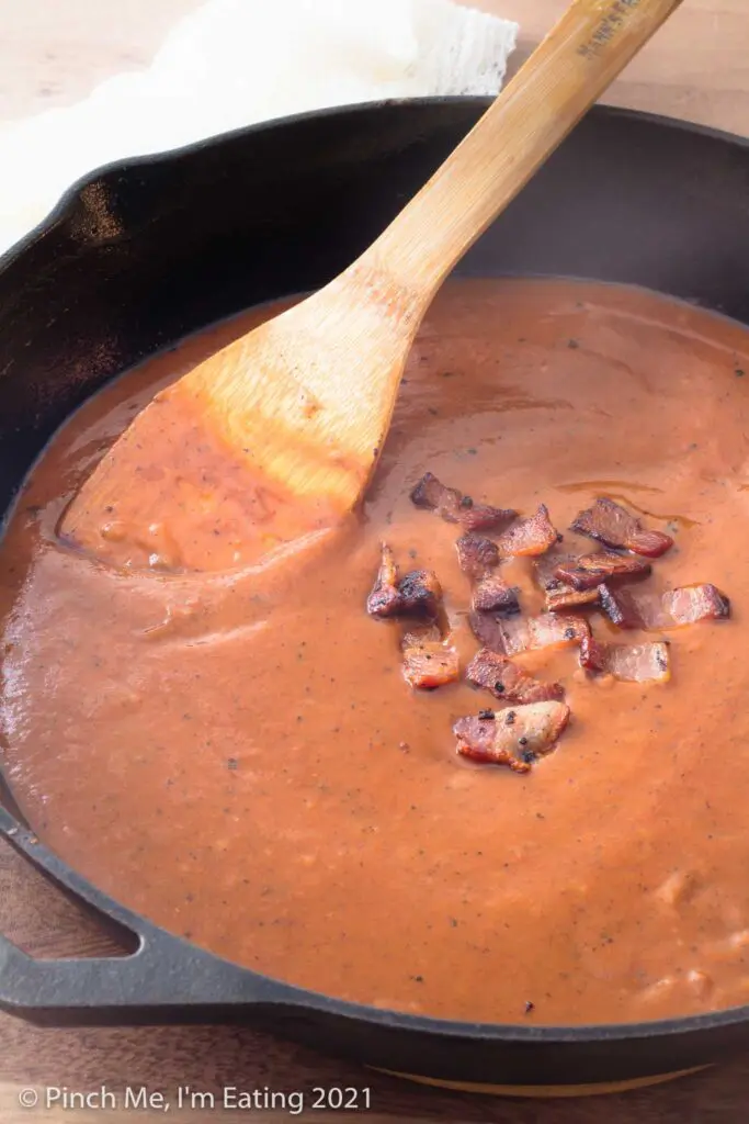 Southern tomato gravy in a cast iron skillet with wooden spoon and bacon pieces