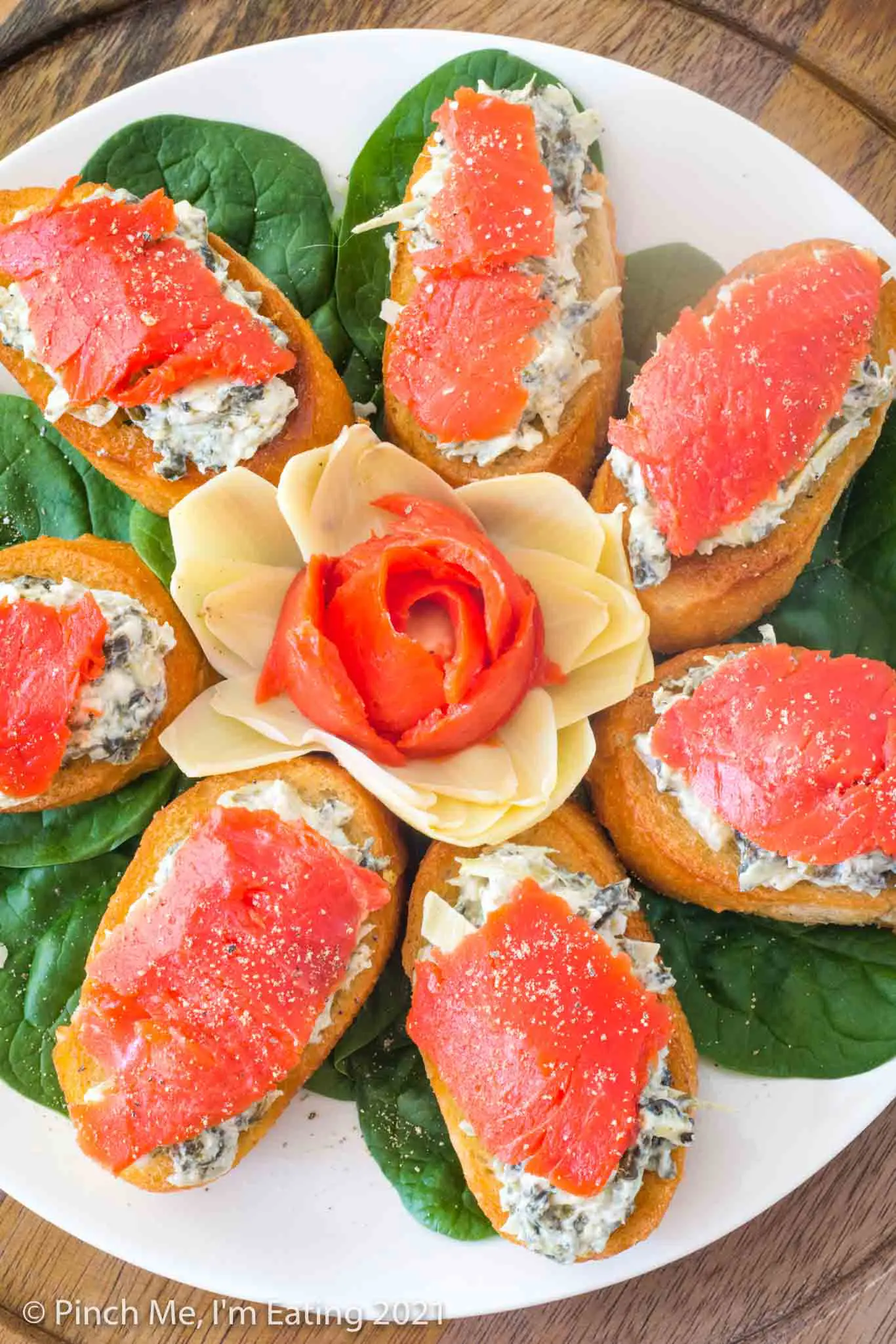 Spinach artichoke dip crostini with smoked salmon arranged in on a white plate around a flower made of artichoke heart and smoked salmon