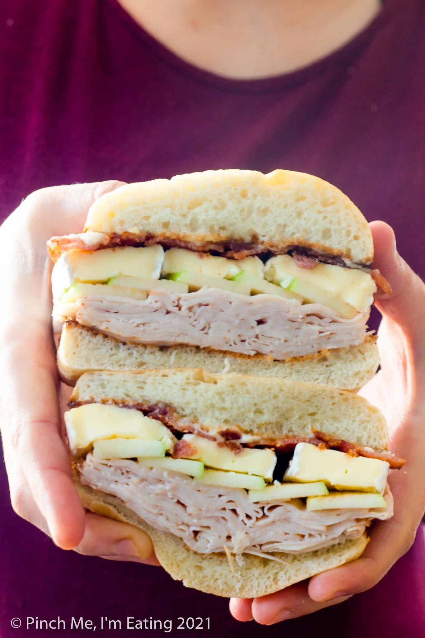 White woman holding a smoked turkey, bacon, and brie sandwich cut in half