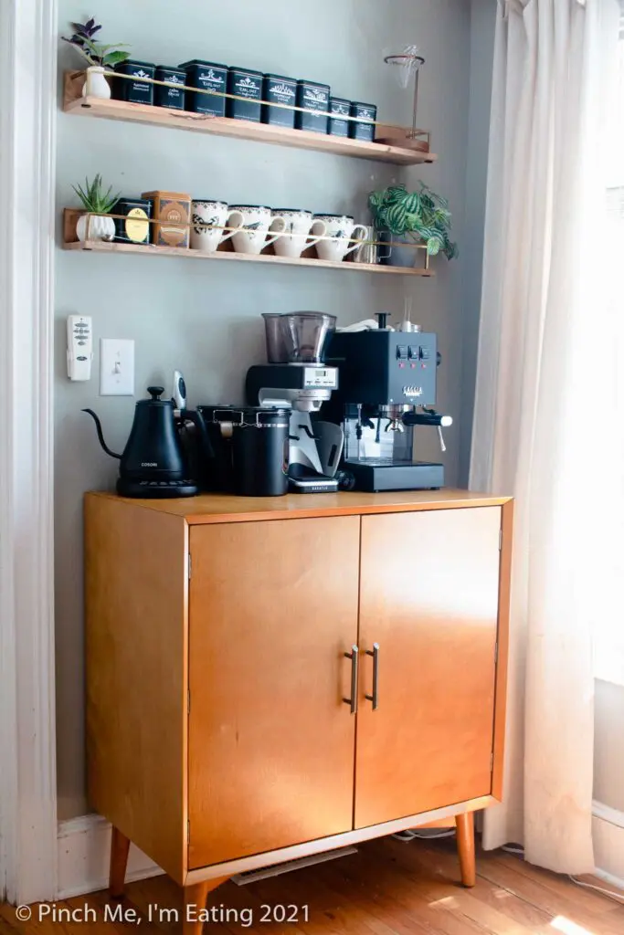 Modern DIY kitchen coffee bar station cabinet with floating shelves, mugs, tea tins, espresso machine, and electric kettle