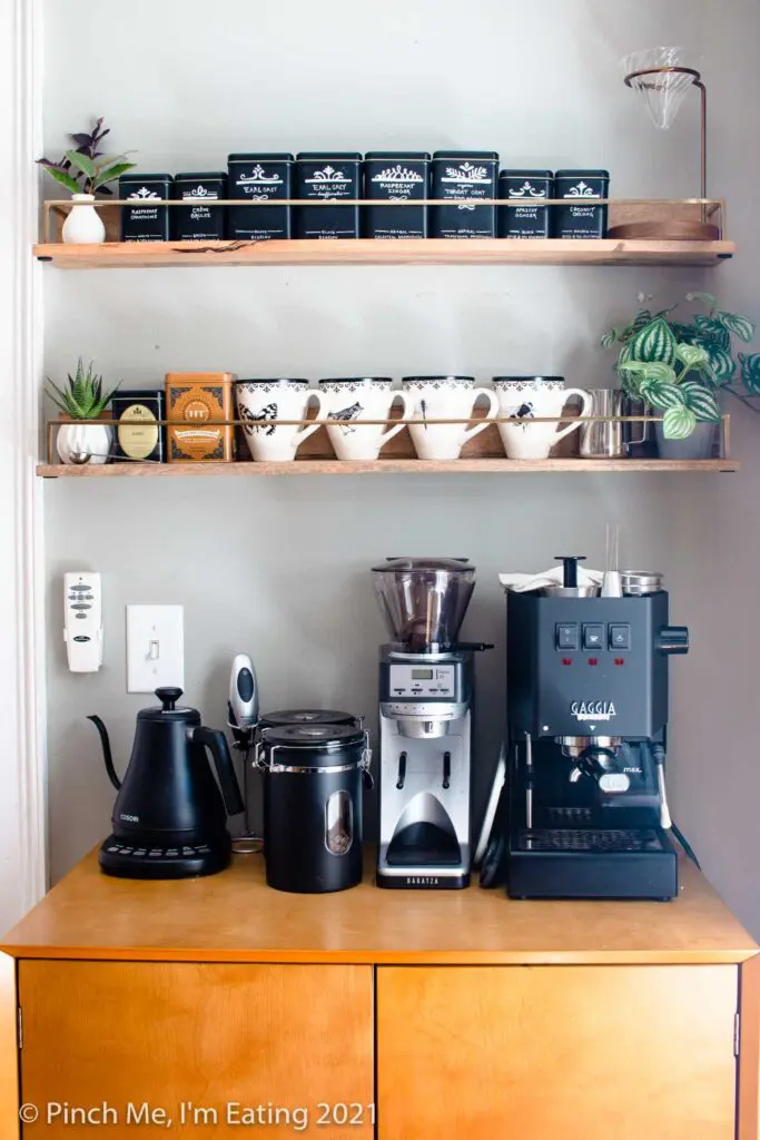 Modern DIY kitchen coffee bar station cabinet with floating shelves, mugs, tea tins, pourover stand, faux succulents, espresso machine, coffee canisters, and electric kettle