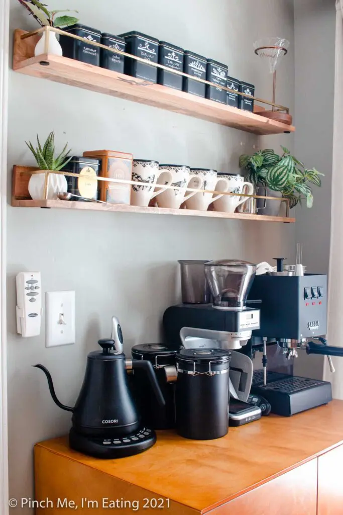 Modern DIY kitchen coffee bar station cabinet with floating shelves, mugs, tea tins, pourover stand, faux succulents, espresso machine, coffee canisters, and electric kettle