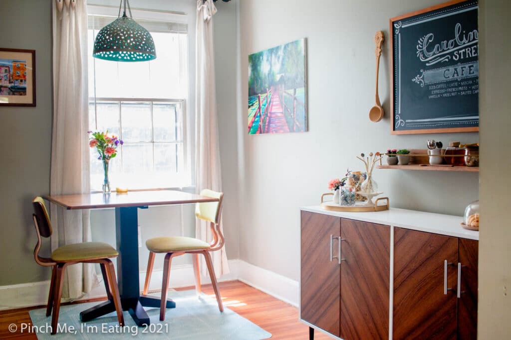 Cafe table in dining room next to window with pendant light and fresh flowers and DIY home coffee bar station on a buffet table with floating shelf and menu chalkboard