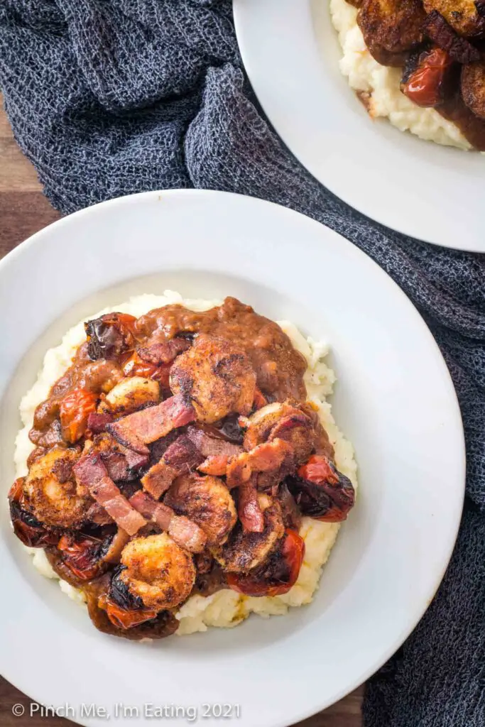 Overhead view of shrimp and grits with tomato gravy and bacon pieces in a white bowl