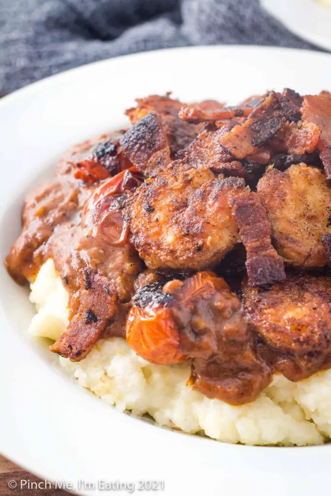 Closeup side view of shrimp and grits with tomato gravy and bacon pieces in a white bowl