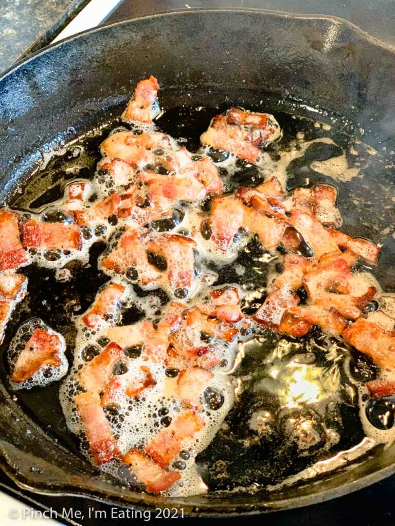 Cut up bacon pieces frying in a cast iron skillet
