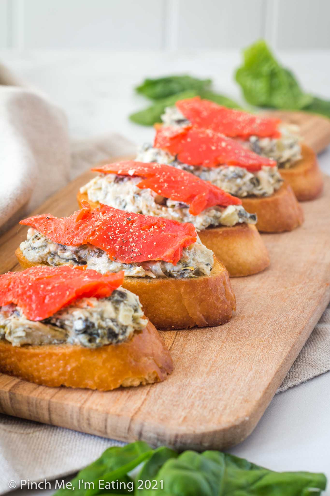 Spinach artichoke crostini with smoked salmon on a wooden cutting board