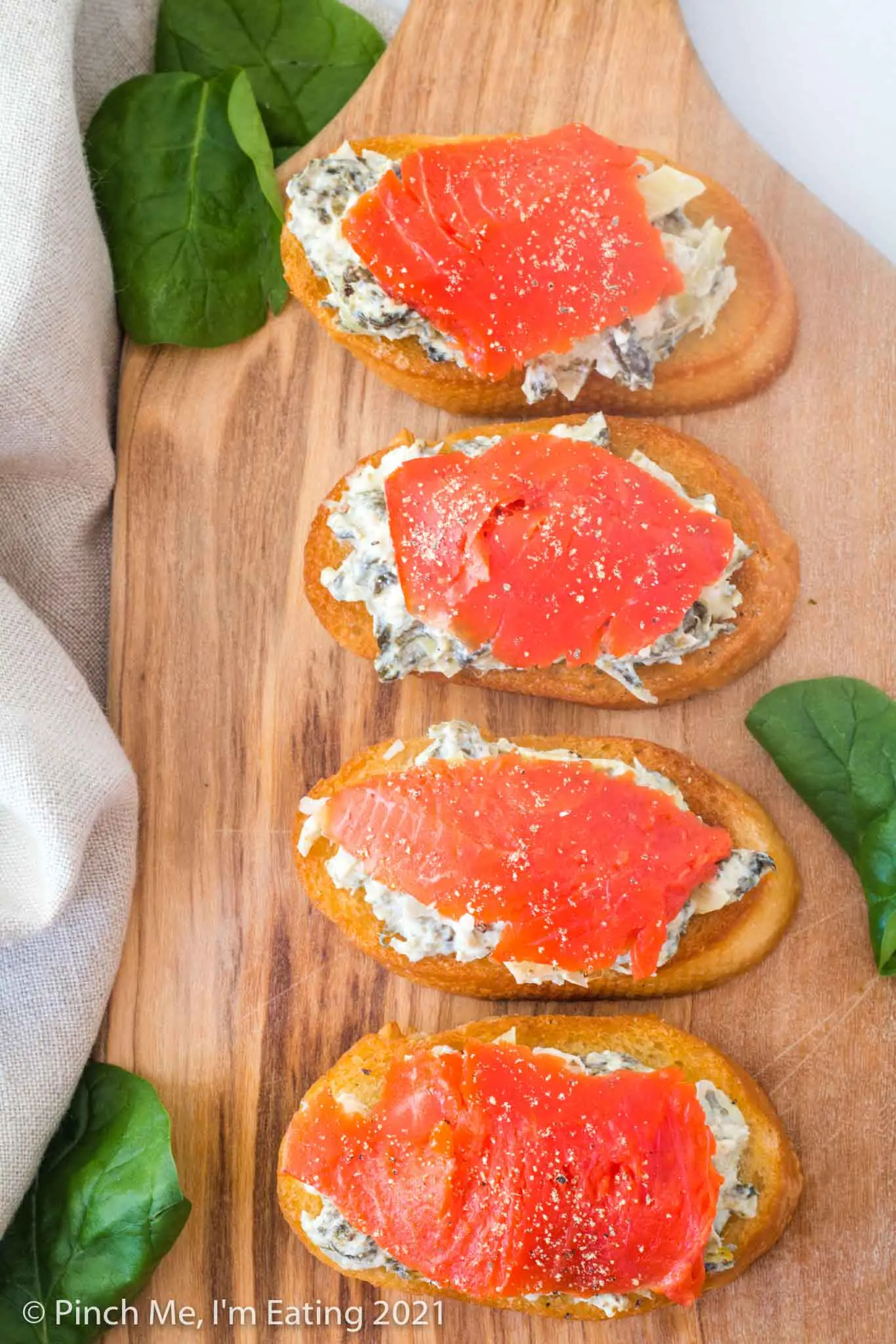Artichoke spinach dip crostini with smoked salmon on a wooden cutting board