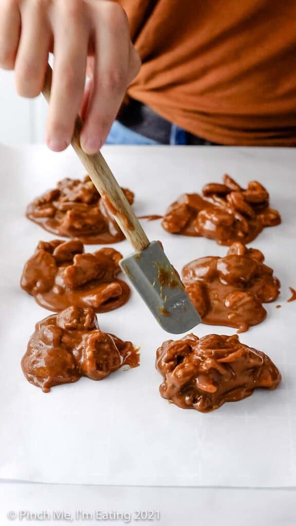 Spatula scooping hot pecan pralines onto parchment paper.