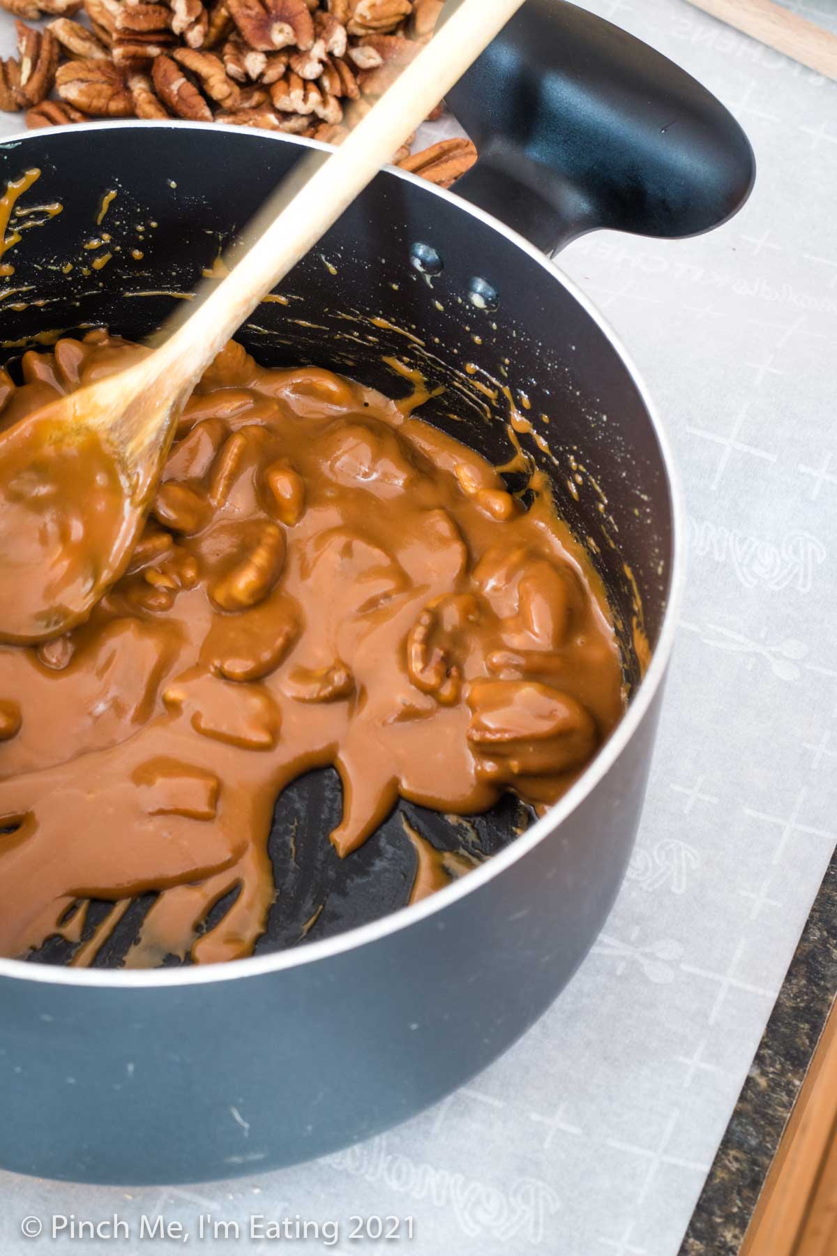 Pot full of pecan praline candy mixture with a wooden spoon.