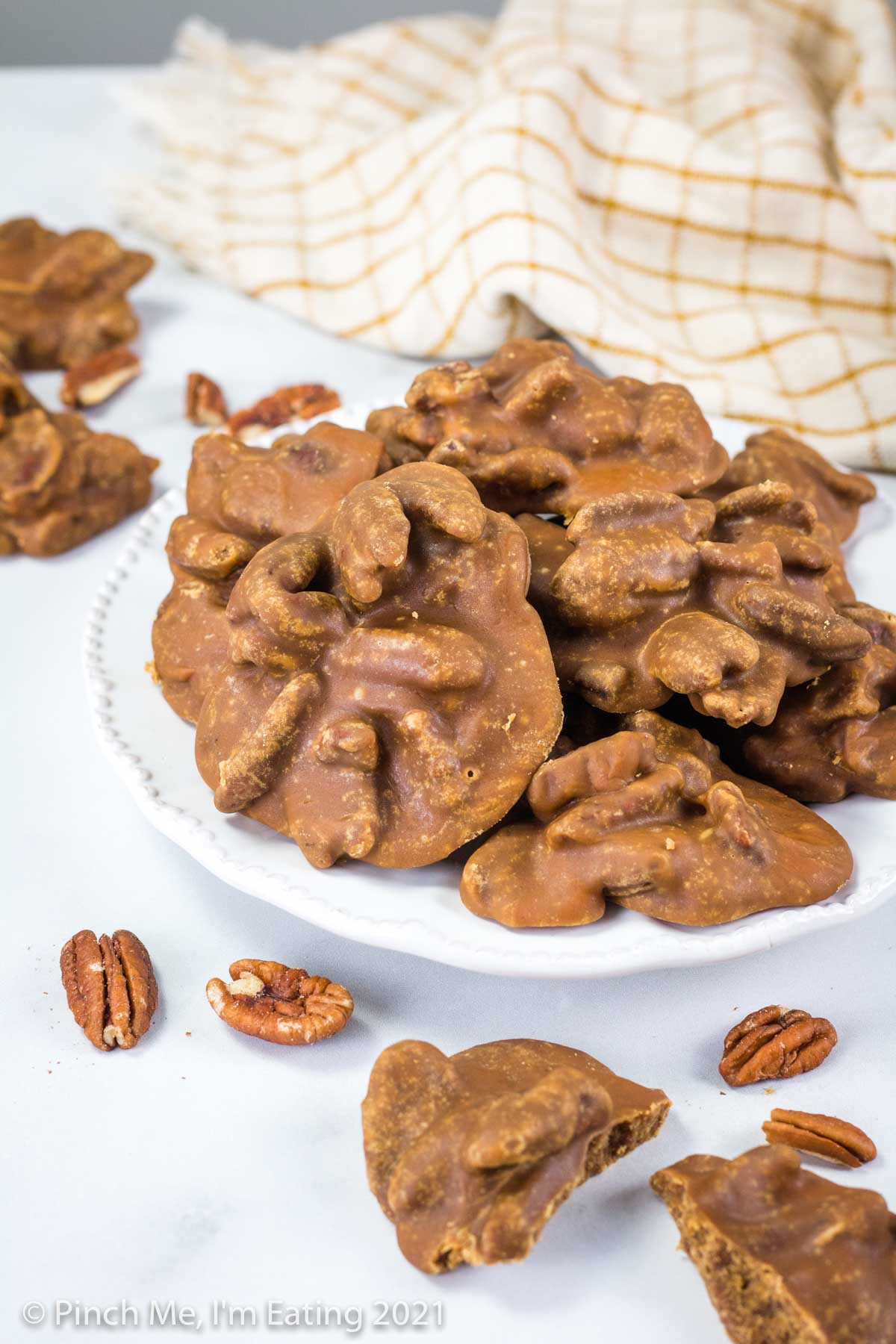 Southern pecan pralines on a white plate with a kitchen towel in the background.
