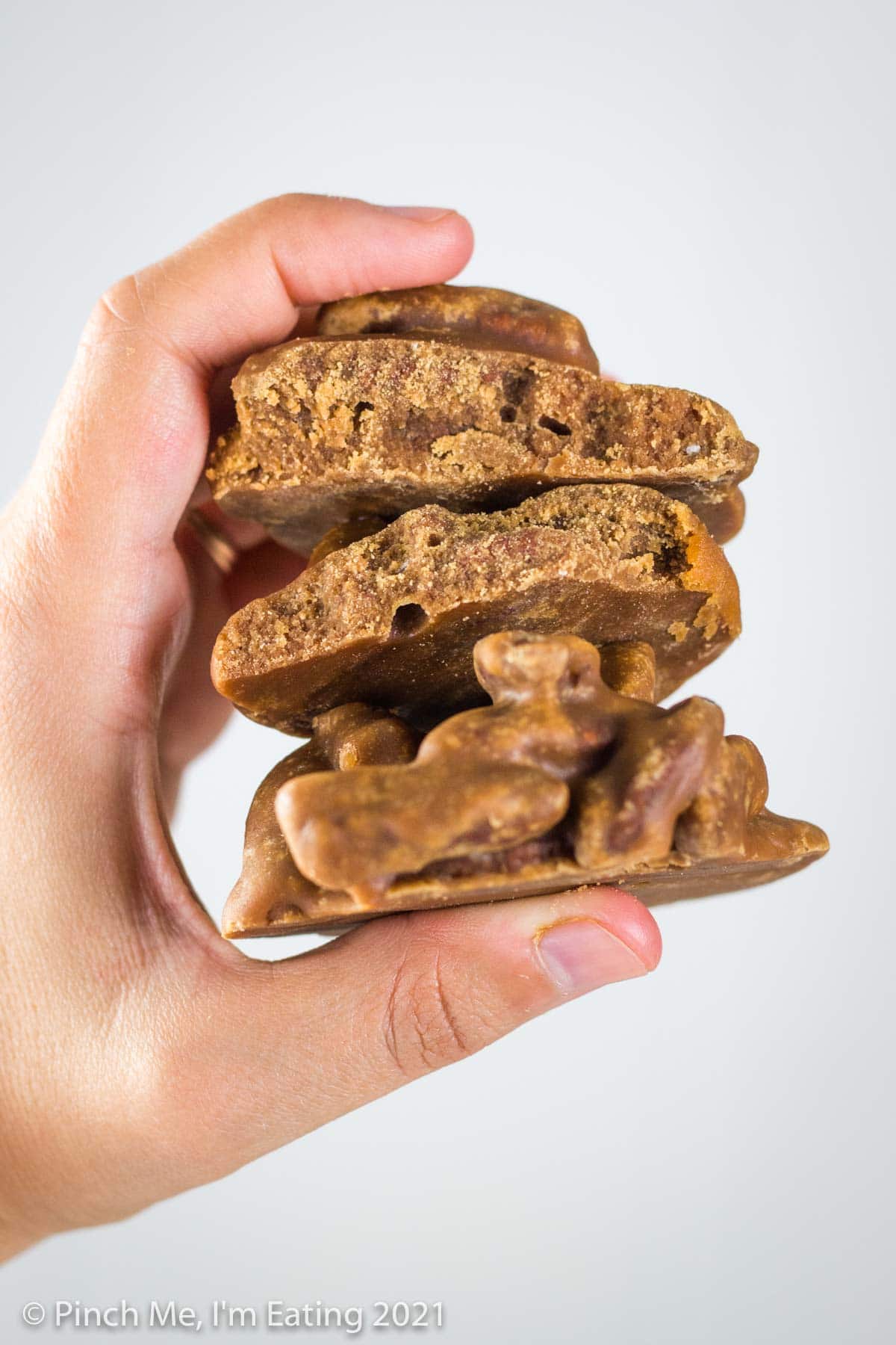 A hand holding a whole Southern pecan praline and one broken in half to show inner texture.