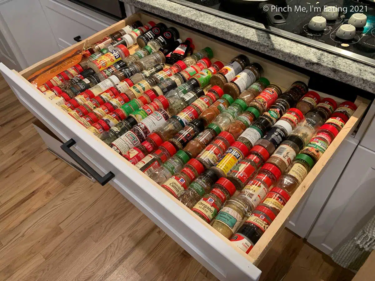 Cluttered, disorganized spices lined up in a drawer in their original containers