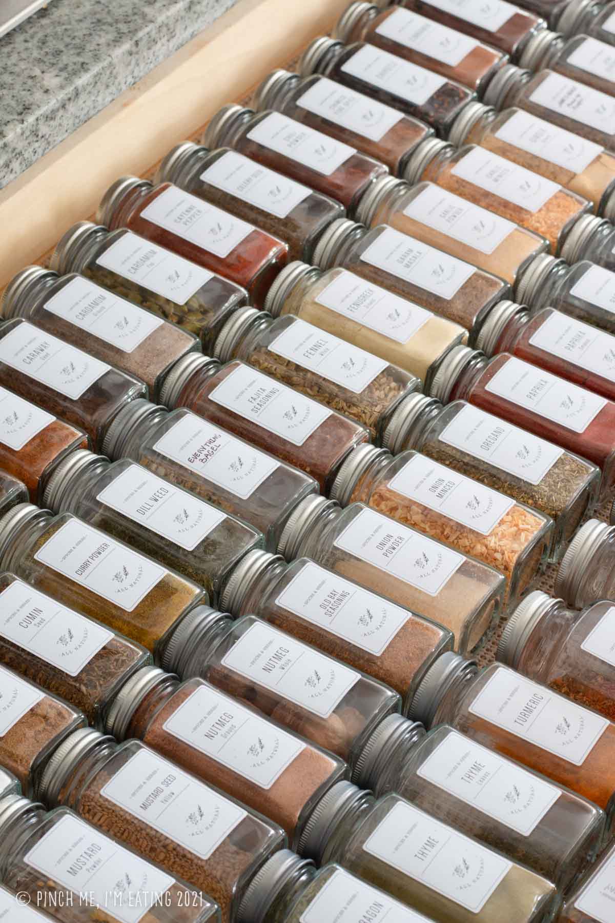 Spices in matching glass jars with white labels lined up in a drawer
