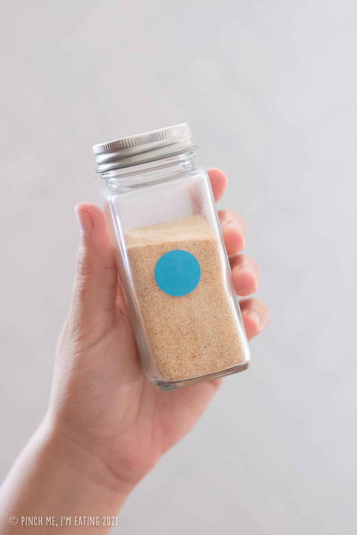 Hand holding glass jar of garlic powder with round blue sticker to denote backstock is available