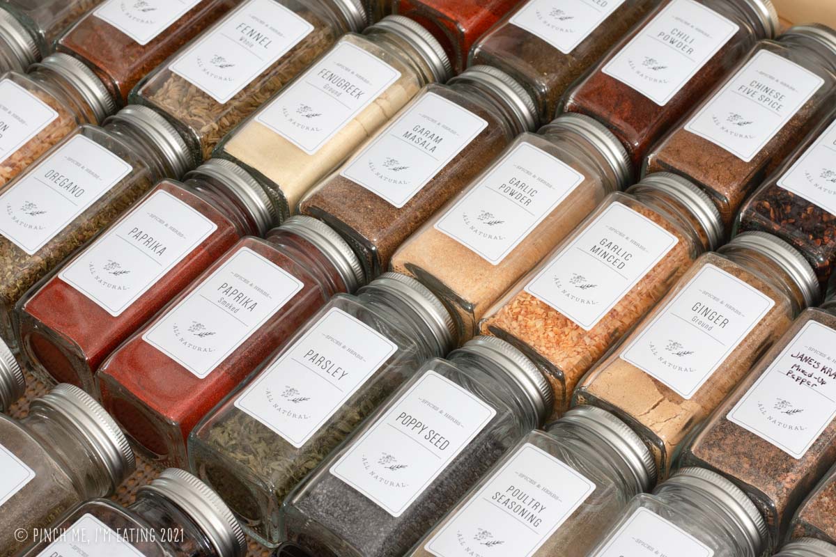 Closeup of spices in matching glass jars with white labels lined up in a drawer